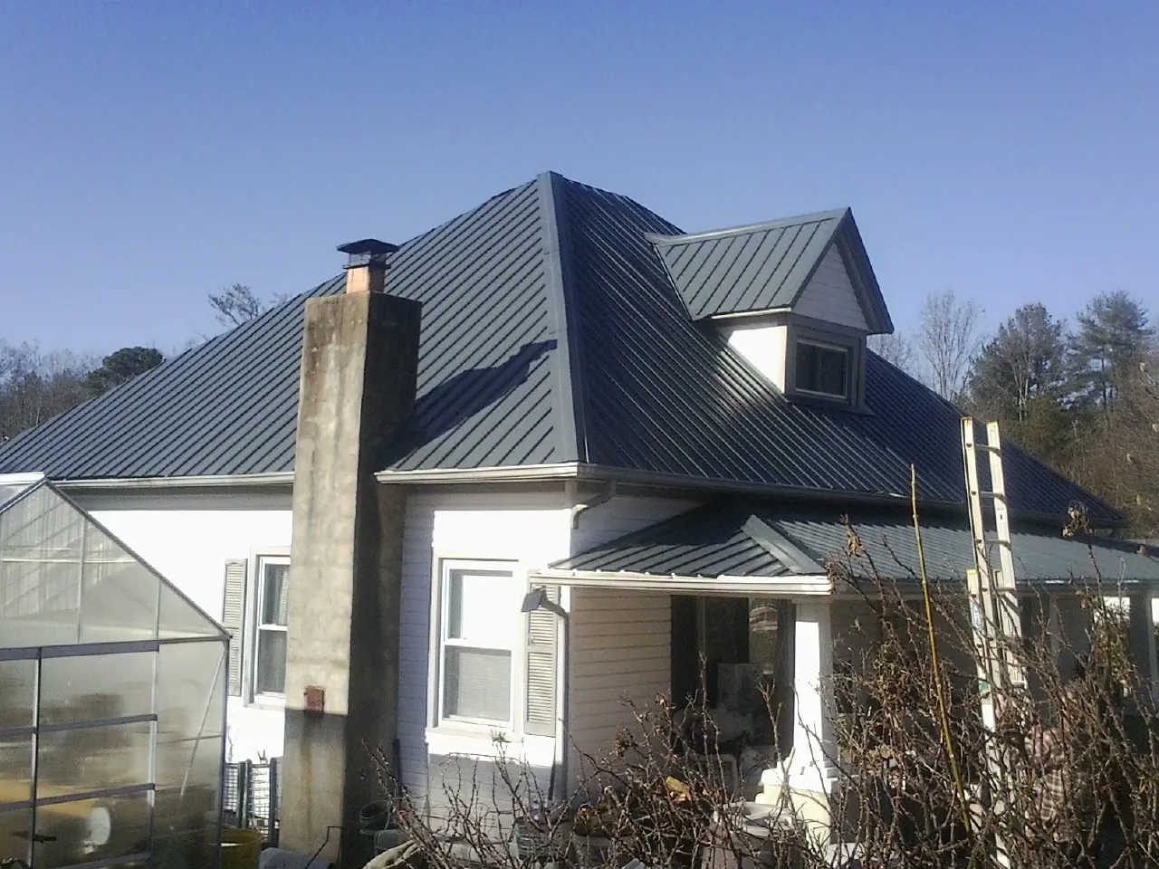 Dark blue standing seam metal roof on a white farmhouse with dormer — Slate & Tile Roof Repair by Roofing Brothers in Portis