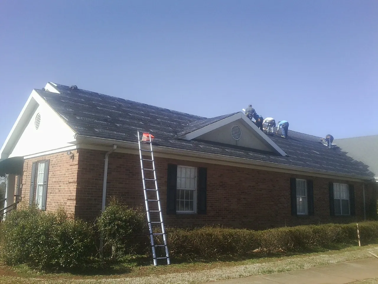Crew tearing shingles off a brick ranch roof with a ladder set — Metal Roof Repair work by our crew in Portis