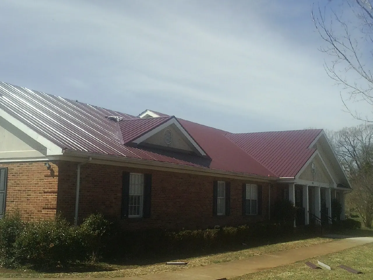 Red metal roof with gabled entries on a long brick building, from a Hail Damage Roof Repair job in Portis