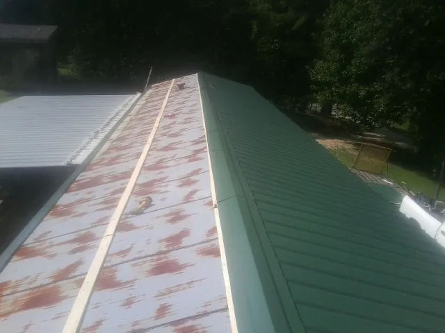 Old rusted panels beside newly installed green metal roofing — Wind Damage Roof Repair by Roofing Brothers in Portis