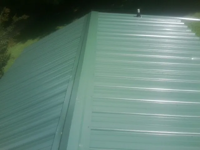 New green metal panels meeting at the ridge of a roof — Flat Roof Repair work by our crew in Portis