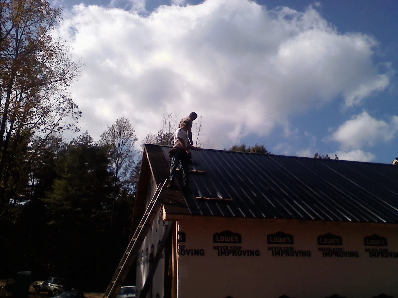 Roofer fastening dark metal panels high against a cloudy sky, from a Roof Inspection job in Portis