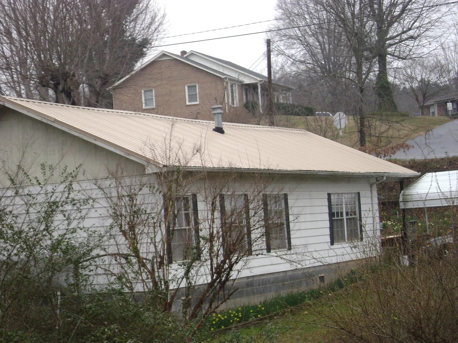 Tan metal roof on a white sided house set into a hillside — Commercial Roofing by Roofing Brothers in Portis