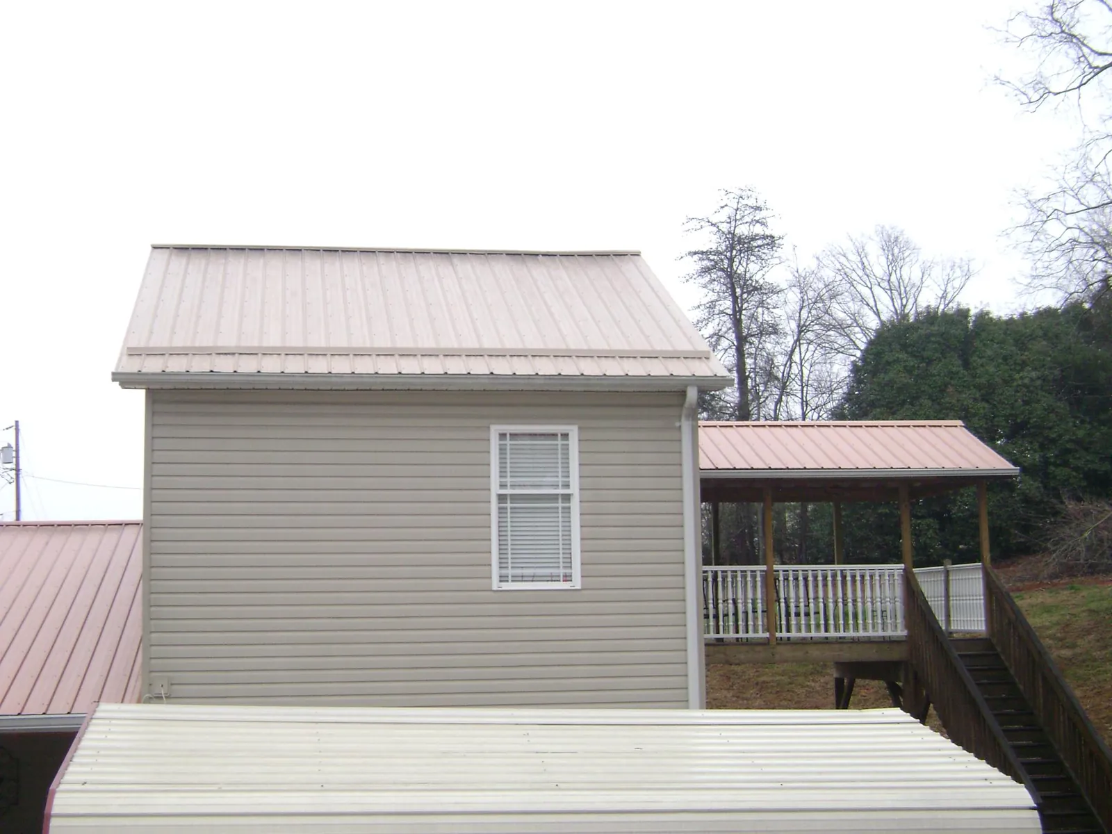 Tan metal roofs on a two story addition and attached porch, from a Roof Replacement job in Portis